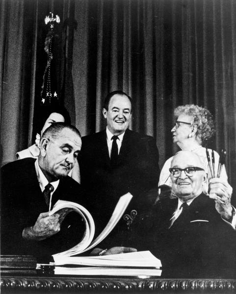 President Lyndon Baines Johnson signs the Medicare bill. Former President Harry S. Truman, "who started it all," is present with Mrs. Bess Truman, Hubert Humphrey, and Mrs. Lady Bird Johnson. Johnson was the 36th United States President, from 1963-1969.