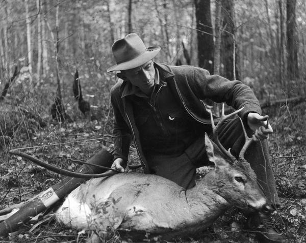 Bow-hunter Fred Bear poses with his bow and a deer carcass.