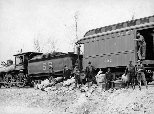 A deer hunting party pose with carcasses and supplies by a train on the C. St. P. M. & O. railroad.