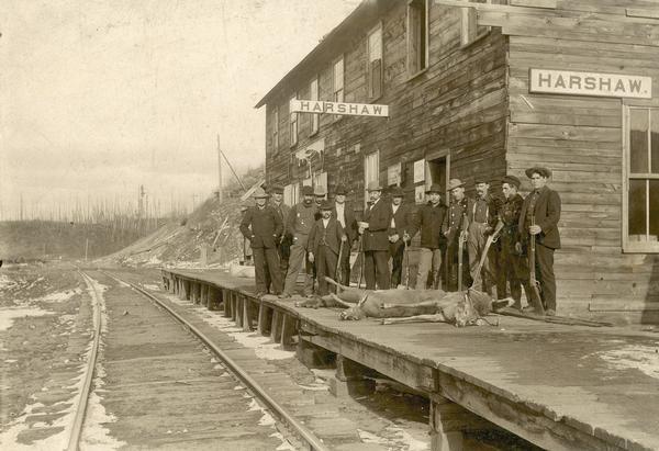 A group of men pose with guns and deer carcasses on the railroad platform at Harshaw.