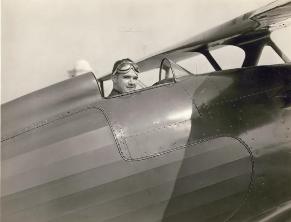 Howard Hughes - aviation-obsessed motion picture producer, millionaire playboy, and aircraft business leader - seated in the cockpit of his airplane after a test flight.  In this plane, a Boeing pursuit plane of the Army type, powered with a Wasp-Whitney 580-horsepower engine which he had remodeled to meet his specification, Hughes had already averaged over 225 miles per hour.