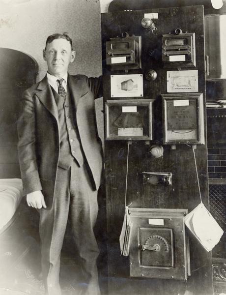 A man shows off an incandescent lamp switchboard with bamboo filiament, lamp receptacle with wooden base, current and pressure indicators and controlling devices at the electrical plant operated by water power, the first commercial electric lighting plant.