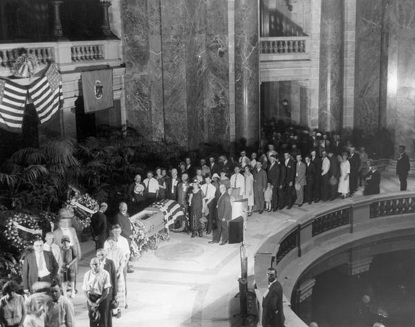 A crowd of mourners viewing the flag drapped casket of Senator Robert M. La Follette, Sr., in the Wisconsin State Capitol rotunda.