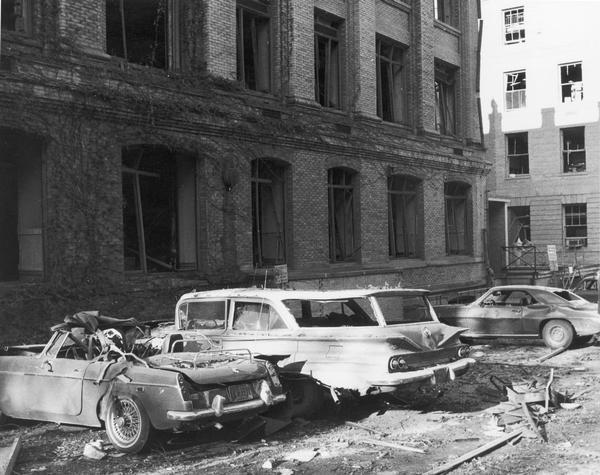 Aftermath of the bombing of Sterling Hall on the University of Wisconsin campus. The view includes three heavily damaged cars that were next to the building at the time of the explosion.  Unfortunately, despite an attempt to detonate the bomb when the building was vacant, a physics researcher conducting research unrelated to Army Math Research Center, was killed in the explosion. The sobering impact of Robert Fassnacht's death brought a sudden halt to the violence to which anti-war protesters and police had resorted. 