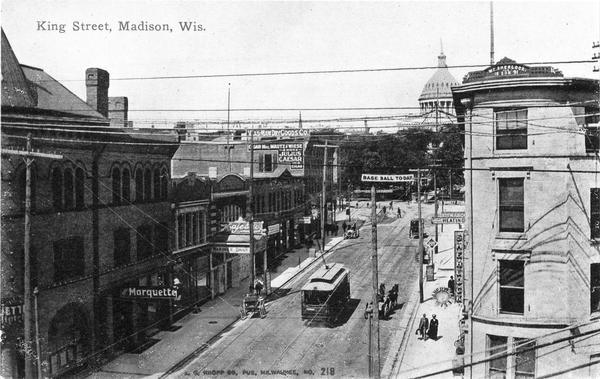 Looking down King Street with streetcar. A sign that reads, "Base Ball Today" is strung over the street and the Wisconsin State Capitol is in the background.