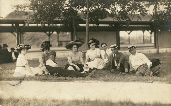 A group of well-dressed people at repose on the grass, possibly having a picnic. Second from left is Alma Reinhardt Taylor.