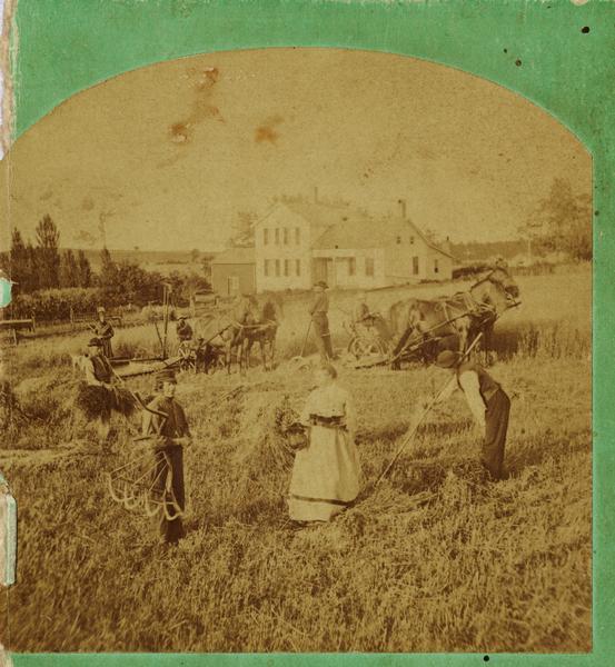 A woman stands in the middle of a field with men around her working with tools. A house and horse-drawn tractor are also seen.