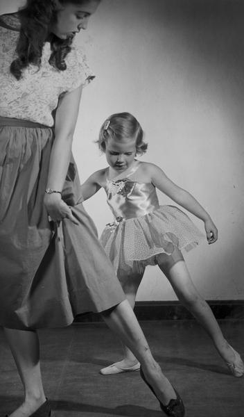 Virginia Lee Kehl, a third generation of the Kehl family involved in dance instruction in Madison, demonstrates a ballet "tendu" to a young dancer in costume.