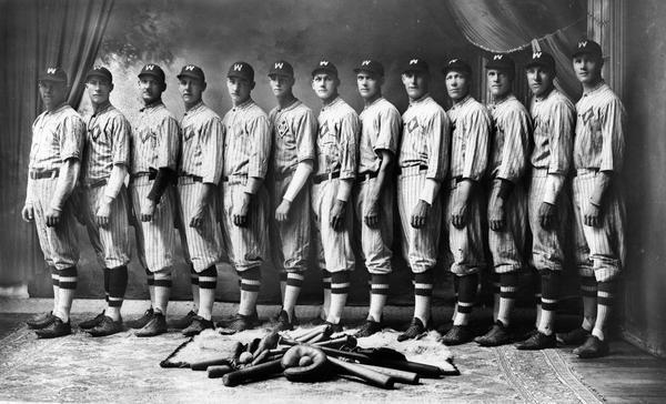 Studio portrait of Wittenberg Grays baseball team in uniform with balls, bats and gloves in foreground. Third player from the left is Melvin Schlytter (catcher).