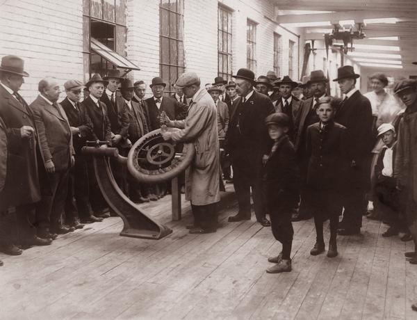 Interior shot of a group of men, women and boys at the Gillette Tire Company. The Gillette Safety Tire Company was founded in Eau Claire in 1916 and the crowd is probably present to witness the production of the first experimental tire on May 23, 1917.