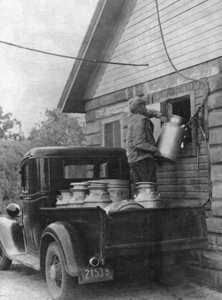 A man unloads milk cans from a Ford Model T pickup truck at a creamery receiving station.