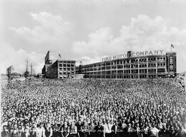 Thousands of employees appear in a composite photograph representing 50,000 employees of the Ford Motor Company. A company building reading "Ford Motor Company" can be seen behind the crowd. Text on photograph reads: "Part of 50,000 employees- Ford Motor Co. Detroit, Mich."