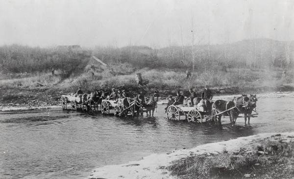Crossing a river on the way to Vermillion Lake in the early 1880's, before the building of any railroads in that part of the country. The teams were part of the road crew that had improved the Vermillion Trail for possible summer traffic.