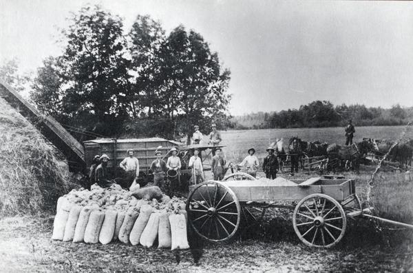 Sweep horsepower threshing. Men and products lined up near the machinery with a large haystack on the left.
