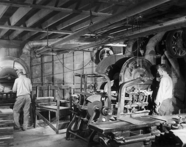 Two employees of the Hess Cooperage, working at machines that are milling oak lumber into staves for barrels.