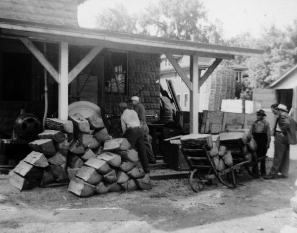 Two employees of Hess Cooperage, working at their outdoor sawmill behind the cooperage, quarter sawing oak logs to be made into barrel staves and heads with three men looking on.