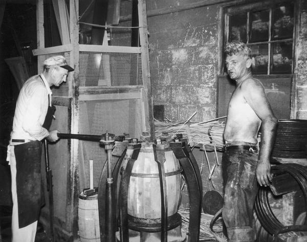 Frank "Foots" Hess Jr. and Tony Hess using a truss hoop driver to install hoops around a barrel at the Hess Cooperage. Also known as "trussing".