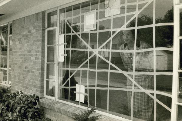 Daisy Bates, an American civil rights activist, publisher and writer who played a leading role in the Little Rock integration crisis of 1957, looking through a broken window repaired with tape.