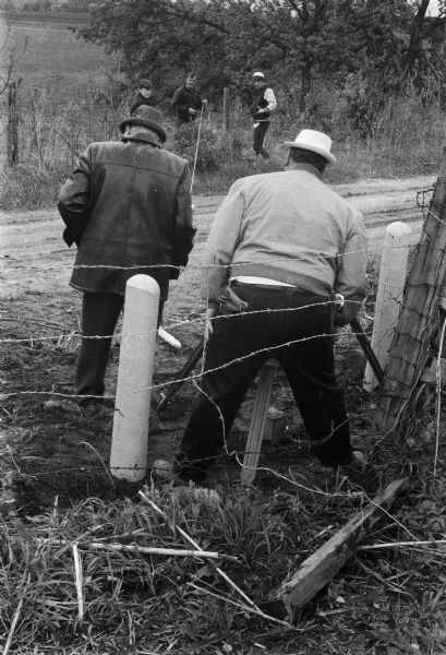 Five men surveying land across a road. They're standing near a barbed wire fence.