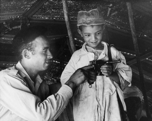 A man shows a little boy (his son?) a gun.