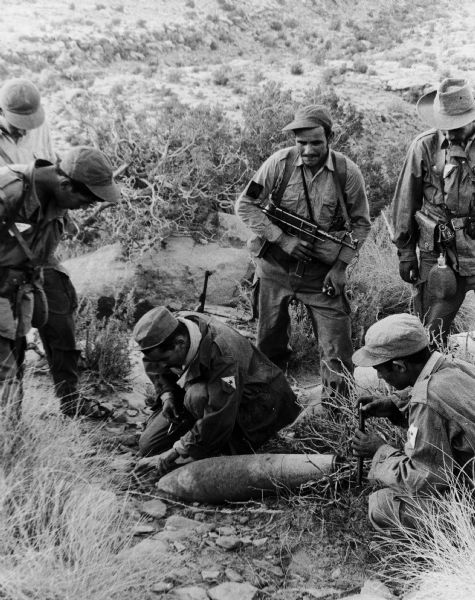 A group of men from the National Liberation Front (FLN) show an unexploded aerial bomb to Dickey Chapelle, demonstrating NATO involvement in the war.