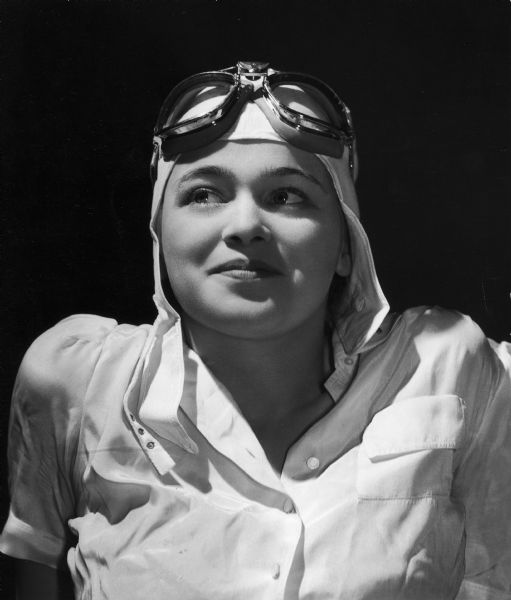 Portrait of Dickey Chapelle wearing a white shirt, white flight headgear and goggles.