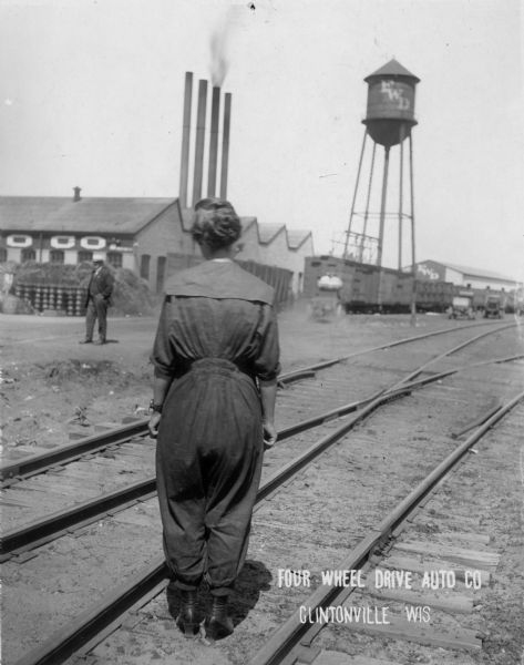 Woman worker with her back turned to the camera standing in front of the Clintonville Four Wheel Drive factory.
