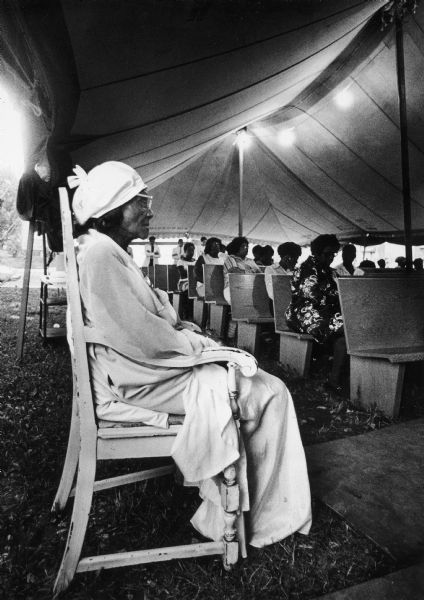 Willie Mae Small, 107 years old, sits in a chair off to the side during an outdoor service (church?).