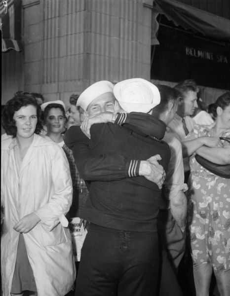 Crowd with two sailors hugging each other. Sailor with his back to the camera is Seabee B. O. Pledger; other sailor is unknown. They are celebrating V-J Day, August 15, 1945, the day on which the Allies announced the surrender of Japanese forces during World War II.