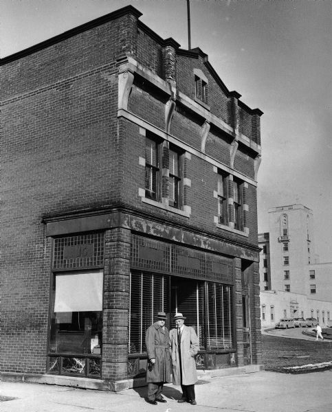 University President E.B. Fred and former governor Oscar Rennebohm posing in front of the first Rennebohm Drug Store in the 1300 block of University Avenue. During the course of its history this building was also the Badger Pharmacy, which Rennebohm purchased about 1912 after it went into bankruptcy, and the original Silver Dollar Saloon. It was later used by the University of Wisconsin-Madison Medical School, which is in the background.
