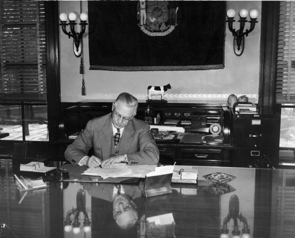 Governor Oscar Rennebohm seated at a desk in the governor's office in the Capitol signing a bill.  Rennebohm, the founder of the Rennebohm Drug Store chain in Madison, served as governor from 1947, when he succeeded to the unexpired term of Walter Goodland, until 1951.