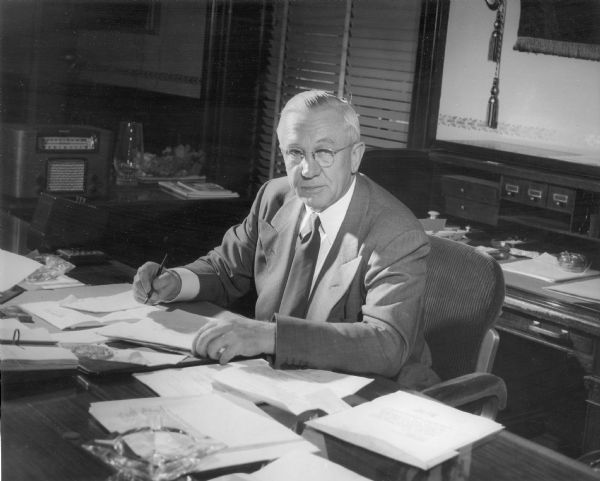 Portrait Governor Oscar Rennebohm seated at a desk in the Capitol doing paperwork.