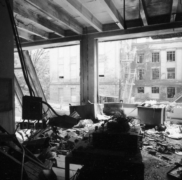 A view looking out from the ground floor of Sterling Hall after the building was bombed.  Unfortunately, despite an attempt to detonate the bomb when the building was vacant, a physics researcher conducting research unrelated to Army Math Research Center, was killed in the explosion. The sobering impact of Robert Fassnacht's death brought a sudden halt to the violence to which anti-war protesters and police had resorted. 