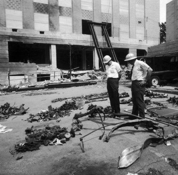 Two men in hard hats observe the ruins of Sterling Hall after it was bombed.  Unfortunately, despite an attempt to detonate the bomb when the building was vacant, a physics researcher conducting research unrelated to Army Math Research Center, was killed in the explosion. The sobering impact of Robert Fassnacht's death brought a sudden halt to the violence to which anti-war protesters and police had resorted. 
