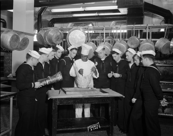 Ten Navy cooks and bakers watching meat carving demonstration by Chef Carson Gulley, UW residence hall chef. Soldiers include Robert W. Merryman, Vernon R. Snyder, Stan Scymanski, Donald Lee, Harry G. Laubhan, Warren E. Lowstetter, Alvin L. Skow, and Vincent J. Lipusz.