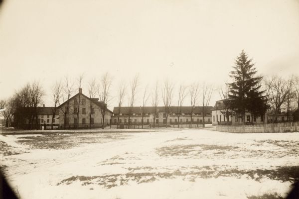 Esterly Harvesting Machine Company looking north across Milwaukee Street. Buildings shown include the Packing and Shipping Department (far left), the Paint Shop (left center), the Pattern Shop (near center), and the company office behind the pine tree.