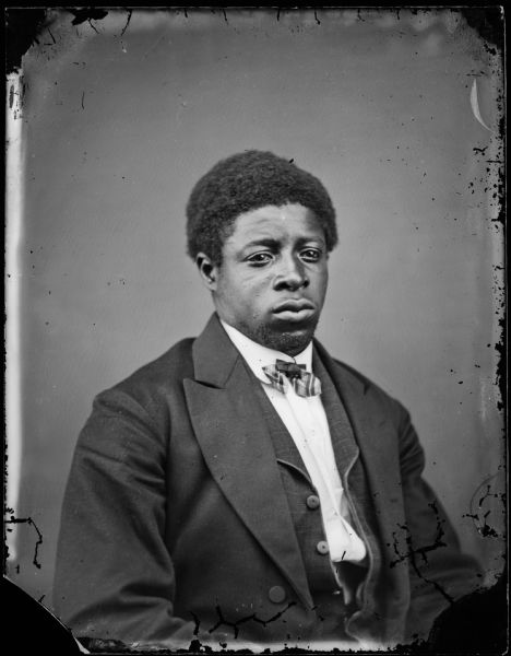 Portrait of an African American man in a shirt, unbuttoned vest and jacket and a striped bow tie.