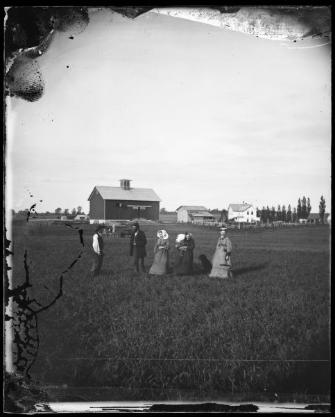 H. Sveren farm with the family standing in the foreground and a dog, farm buildings and fences in the background.