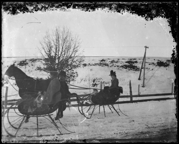 Two cutter sleighs on a road. Cutters were light weight sleighs that carried two passengers.  This photograph shows bare ground in the background that means that the sleighing season was almost over.  The end of sleighing was always a time of regret for Wisconsinites during the nineteenth century because of the comparatively fast speeds of which sleighs were capable.