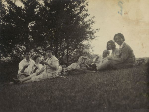 Frank Lloyd Wright lounges on a hill near Spring Green with Kameki and Nobu Tsuchira and four other people, whose identities are unclear, eating watermelon.