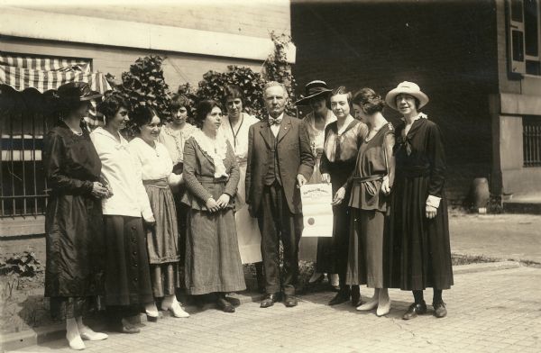 Former Wisconsin State Senator David G. James, Republican from Richland Center (1908-1912) and the father of suffragist Ada James. The photograph was likely taken June 13, 1919 after James delivered Wisconsin's ratification of the 19th Amendment in Washington, DC. James is surrounded by suffragists at the National Woman's Party headquarters building at 14 Jackson Place. The document he is holding is his appointment by Governor Philipp as Special Courier to deliver the ratification.