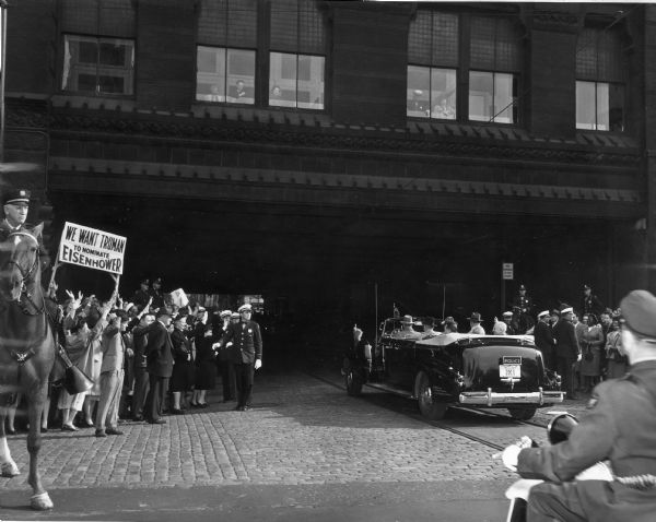 Harry S. Truman being driven in a black limousine to the Democratic Convention. He is waving to onlookers.