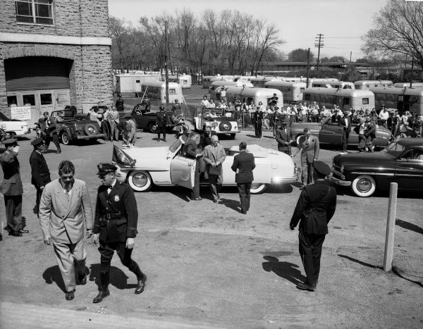 President Harry S. Truman getting out of a car outside the Field House, trailer housing in the background. He came for a 5 1/2 hour visit, gave a "peace" address to the nation from the U.W. Field House and dedicated the new CUNA building on Sherman Avenue. The man in the light-colored suit at left is U.S. Secret Service Agent Gerry Behn. The man directly behind the President on the opposite side of the car is U.S. Secret Service Agent Henry Nicholson. The man with his hand on the back of the car is U.S. Secret Service Agent Floyd Boring.