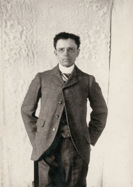 Candid portrait of John Commons posing in front of a lace curtain with his hands in his pockets. This may have been taken while he was at Syracuse University in New York.