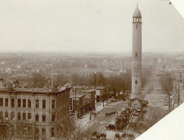 Water tower near East Washington Avenue, that stood from 1890 to 1920. Horse-drawn vehicles are parked at the base of the tower.