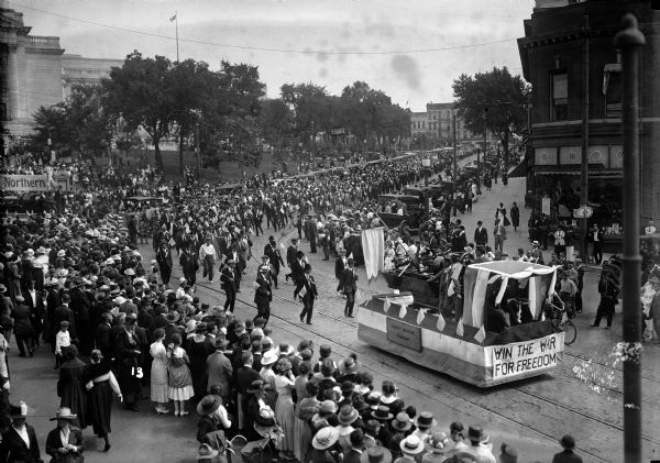 Elevated view of the Labor Day parade on the Capitol Square, at King Street, featuring a float that has the words "Win The War For Freedom" on the front.