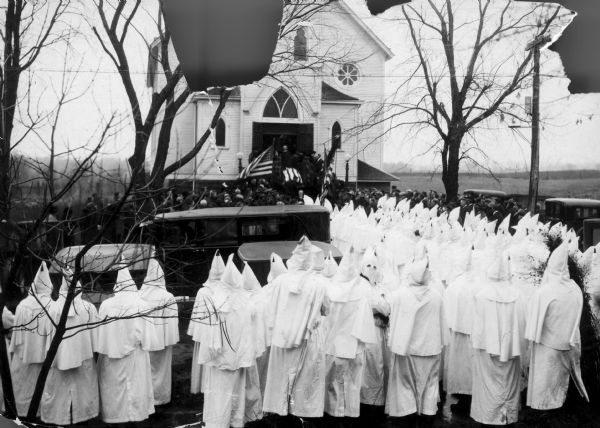 Klansmen of the Ku Klux Klan (KKK) wearing conic masks and white robes gather in front of St. James Lutheran Church, Verona, for the funeral of Herbert C. Dreger, a police officer who was shot and killed in "Little Italy" (South Murray Street). Dreger was shot to death on December 2, 1924.