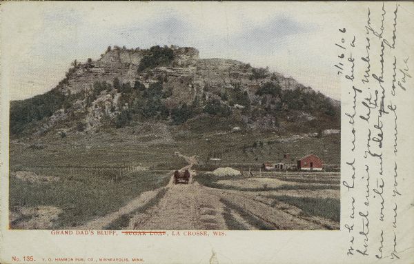 View from road towards farm buildings at the base of the bluff. A horse-drawn vehicle is on the rod. Caption reads: "Grand Dad's Bluff, La Crosse, Wis."
