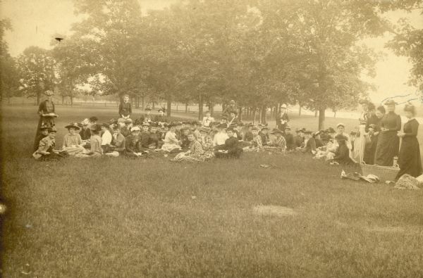 A group of well-dressed women, most of them seated on the grass, gathered for a picnic. They're assumed to be students of Rockford College.