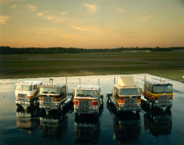 Color studio photograph of five different International Transtar Eagle semi tractors parked on a tarmac at an airfield. The trucks each feature slightly different paint schemes.